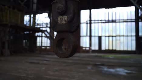 Old-rusty-hook-hanging-in-an-abandoned-spooky-scary-industrial-factory-slightly-moving-at-daylight