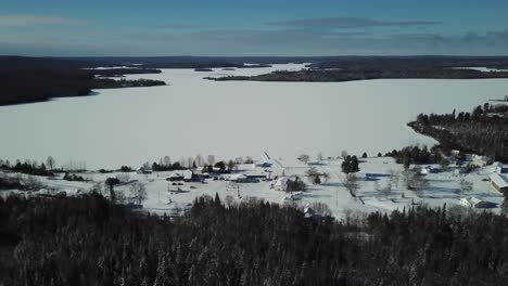 Cold-sunny-blue-sky-winter-day-in-the-northern-countryside-of-Canada---Drone-4k-Aerial-small-town-by-a-frozen-lake