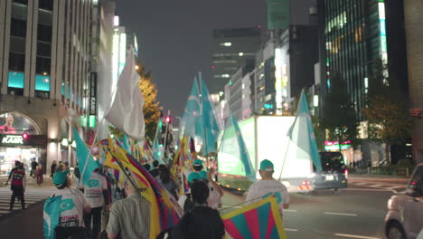 Uyghur-And-Tibetan-Flags-Held-By-Activists-Marching-On-The-Street-In-Tokyo,-Japan-With-Traffic-At-Night---medium-shot