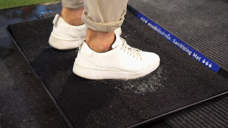 Person-rubs-white-sneakers-on-sanitizing-mat-to-disinfect