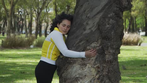 Good-looking-young-brunette-woman-closing-her-eyes-while-hugging-a-tree-in-Palermo-Woods
