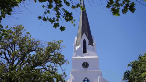 Traditional-Cape-Dutch-Church-tower-appearing-through-oak-trees-in-clear-blue-sky-as-moving-towards-it-in-Stellenbosch