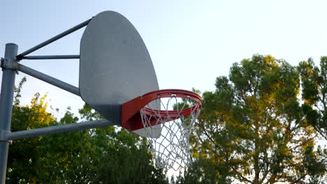 Walking-up-towards-a-basketball-hoop-with-metal-backboard-and-and-orange-rim-in-an-empty-park-court-at-sunrise