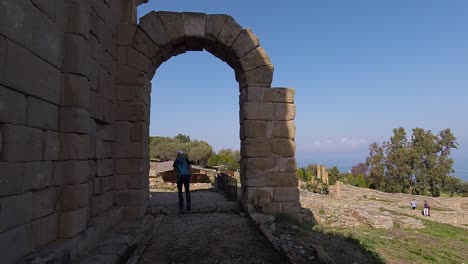 Tourist-walking-under-arch-in-Tinrdai,-Sicily,-Italy