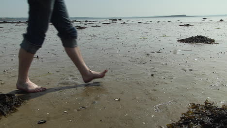 Man-walking-across-wet-beach-bare-foot-at-low-tide