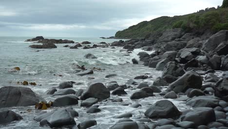 SLOWMO---Waves-hitting-rocks-on-the-beach-in-Bluff,-New-Zealand-on-a-cloudy-day