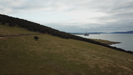 Drohnenschwenk-über-Küstenvorland-Mit-Bohrinsel-Im-Hintergrund-Australien