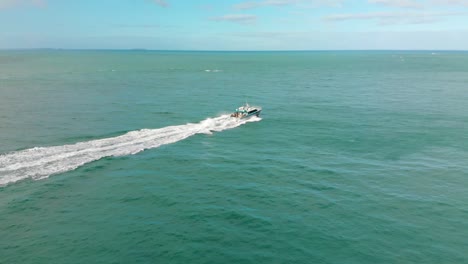 Boat-on-blue-ocean-with-Stewart-Island-in-the-background-on-sunny-cloudy-day---Bluff,-New-Zealand---Aerial-Drone