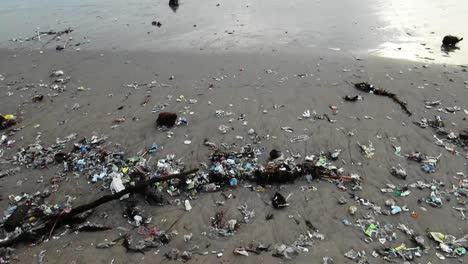 Kippaufnahme-Von-Einem-Stark-Verschmutzten-Strand-Zum-Meer,-Während-Wellen-Müll-An-Die-Küste-Spülen