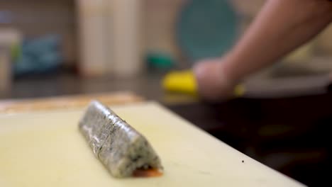 A-cook-cuts-the-triangle-shaped-sushi-roll-into-small-equal-pieces-and-cleans-his-knife-with-kitchen-napkin-after-every-cut