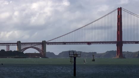 Windsurfista-Distante-Acelera-A-Través-De-Aguas-Turbulentas-Hacia-El-Sol-Frente-Al-Puente-Golden-Gate-En-San-Francisco
