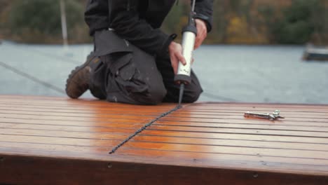 Junger-Mann-Versiegelt-Das-Plankendach-Eines-Holzbootes-Mit-Wasserdichtem-Sika-Flex-Mastix,-Um-Regen-Abzudichten