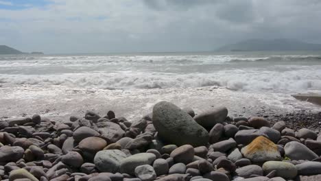 Peaceful-Ocean-Waves-Hitting-Smooth-Grey-Rocks-with-Cloudy-Skies-on-Beach-Medium-Shot