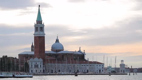 Boats-leaving-the-frame-passing-by-church-of-San-Giorgio-Maggiore-in-Venice,-Italy-at-sunrise