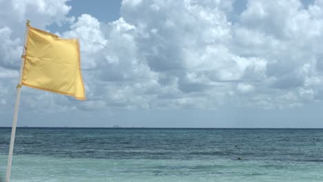 Bandera-Amarilla-Ondeando-En-El-Viento,-Con-Vistas-Al-Océano-Y-Al-Cielo-Nublado