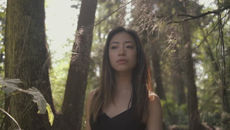 Closeup-of-asian-woman-in-black-looking-forward-and-exploring-sunny-forest,-Slowmo