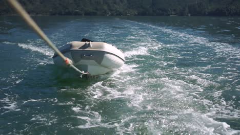 SLOWMO---Inflatable-boat-being-towed-on-rope-behind-boat-on-sea-of-New-Zealand