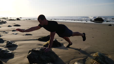A-strong-man-balancing-in-a-yoga-pose-during-a-meditative-workout-at-sunrise-on-a-beach-in-Santa-Barbara,-California-SLOW-MOTION
