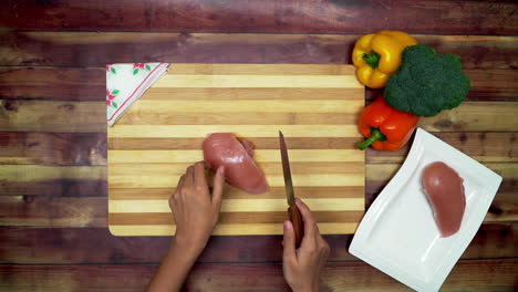 A-Top-view-of-taking-slice-of-a-chicken-from-a-try-to-cutting-board-for-making-slices,-two-big-yellow-and-red-capsicums,-a-boneless-chicken-piece,-grater-and-a-green-broccoli-on-the-table