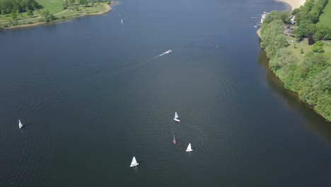 Aerial-footage-of-the-sailboats-with-the-speed-boat-moves-fast-at-the-lake-in-4K