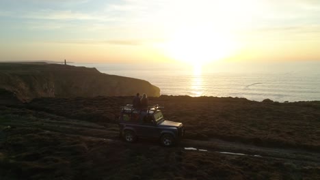 Aerial-of-cute-couple-four-by-four-vehicle-along-ocean-cliffs-at-sunset