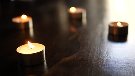 Many-tealight-candles-with-flames-burning-and-dancing-in-slow-motion-with-background-blur-and-light-bokeh
