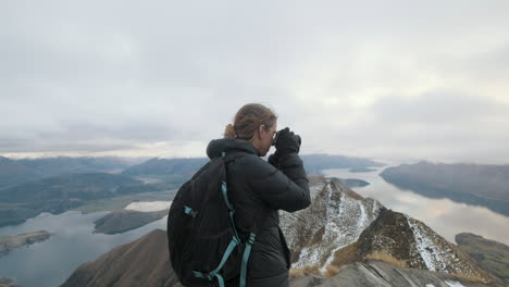 Hiker-taking-photos-at-the-top-of-Roy's-Peak-in-Wanaka,-New-Zealand