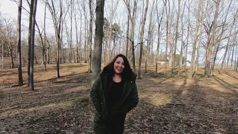 A-young-pretty-teenage-female-walking-through-the-park-laughing-and-shaking-her-head-while-wearing-a-green-coat