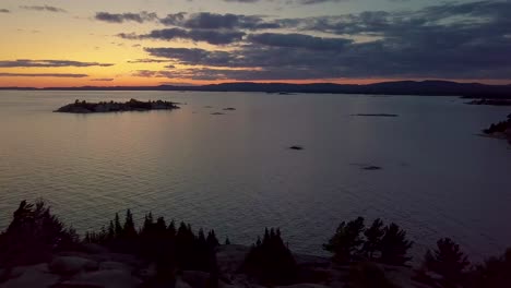 Reveal-of-Rocky-Pine-Tree-Island-in-Big-Lake-just-after-Sunset,-Drone-Aerial-Wide-Dolly-Out