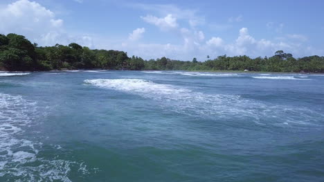 aerial-shot-of-sea-waves-towards-land-and-trees-on-sunny-day