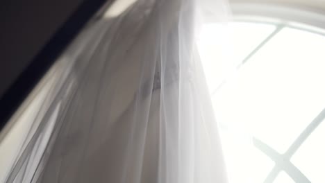 Side-angle-shot-of-a-beautiful-wedding-dress-hanging-from-a-large-church-window-sill---Slow-motion-left-to-right-pan
