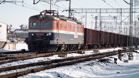 Mitteltotale-Aufnahme-Eines-Elektrischen-Güterzuges,-Der-Tagsüber-Durch-Eine-Schneebedeckte-Stadt-Fährt