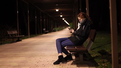 young-woman-alone-looking-their-smart-phone-at-night-in-a-park-bench