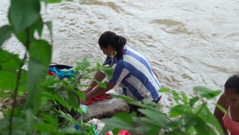 A-woman-washes-and-rinses-her-clothes-while-standing-in-a-river