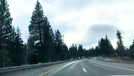Dramatic-Time-lapse-shot-of-a-car-as-it-travels-down-a-country-highway-through-snowy-mountains,-Pine-trees-clouds,-other-vehicles-can-been-seen-in-the-adjoining-lanes
