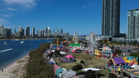 Aerial-view-of-a-colourful-carnival-situated-by-the-sea-with-a-city-skyline-in-the-background
