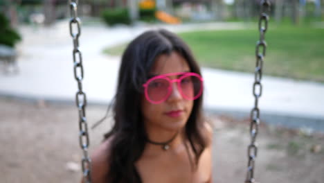 A-beautiful-hipster-fashion-model-wearing-vintage-clothing-and-retro-pink-sunglasses-swinging-on-a-playground-and-having-fun-SLOW-MOTION