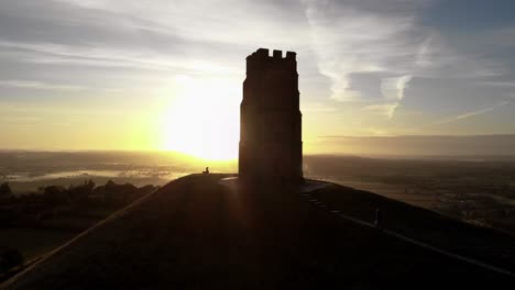 Rising-aerial-shot-of-people-walking-up-Glastonbury-Tor-at-sunrise