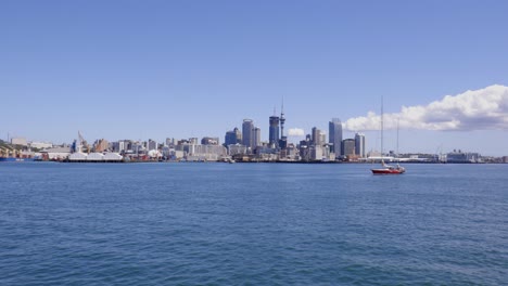 Wide-slow-panning-shot-of-Auckland-city-skyline-and-Commercial-Bay-including-sail-boat-passing,-Auckland,-New-Zealand