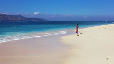Girl-in-bikini-and-snorkel-set-walking-on-white-sand-of-exotic-beach-alongside-beautiful-blue-turquoise-sea-lagoon-preparing-to-dive,-Bali