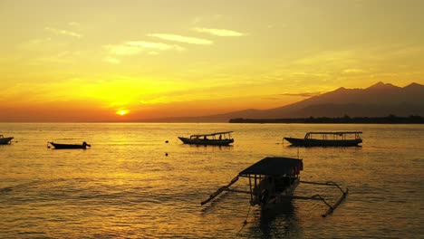 Silhouette-Traditioneller-Balinesischer-Fischerboote,-Die-Auf-Einer-Ruhigen-Meeresoberfläche-Schwimmen-Und-Das-Wunderschöne-Gelbe-Sonnenlicht-Des-Himmels-Bei-Sonnenuntergang-Reflektieren