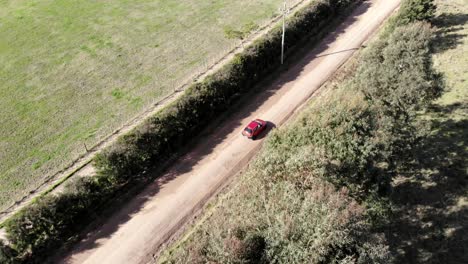 Aerial-Of-Red-Car-Passing-By-On-Small-Country-Road-Rural-Countryside-In-A-Sunny-day