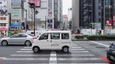 Vehicles-driving-through-an-intersection-on-a-rainy-day-in-downtown-Tokyo,-Japan