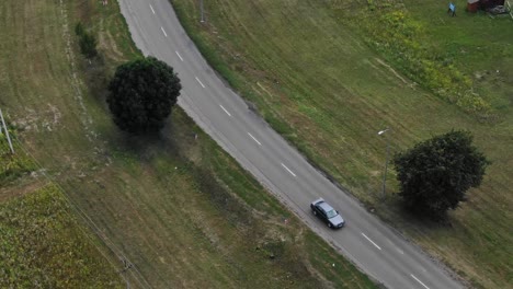 Aerial-View-of-Car-Driving-Down-Road-Surrounded-by-Fields-and-Trees