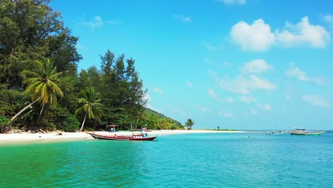 Calm-tropical-beach-with-white-sand-and-palms,-emerald-seawater-with-floating-boats