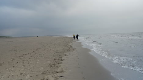 Two-Girlfriends-walking-Along-The-Shore-Of-The-north-sea-during-cloudy-day-on-Texel-Island