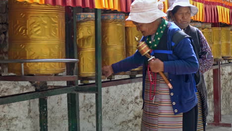 Two-elderly-pilgrims-praying,-spinning-the-golden-prayer-wheels-in-Lasha,-at-the-Potala-Palace