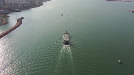 Stückgutschiff-Verlässt-Die-Bucht-Von-Hongkong-Mit-Neigung-Zur-Skyline-Der-Stadt,-Luftaufnahme