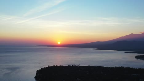 Wunderschöner-Sonnenuntergang-Mit-Buntem-Himmel,-Gelbe-Sonne-Am-Hellen-Himmel,-Der-Sich-über-Der-Ruhigen,-Klaren-Meeresoberfläche-Um-Die-Silhouette-Einer-Tropischen-Insel,-Indonesien,-Spiegelt