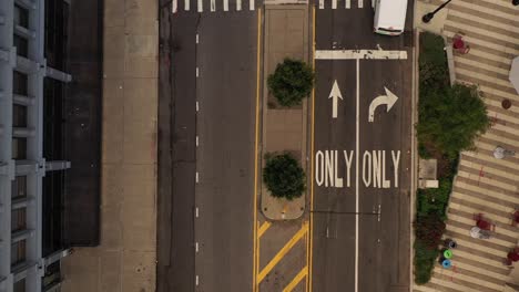 aerial-top-down-view-over-a-median-between-roads,-as-a-few-cars-drive-by-below-on-the-quiet-roads